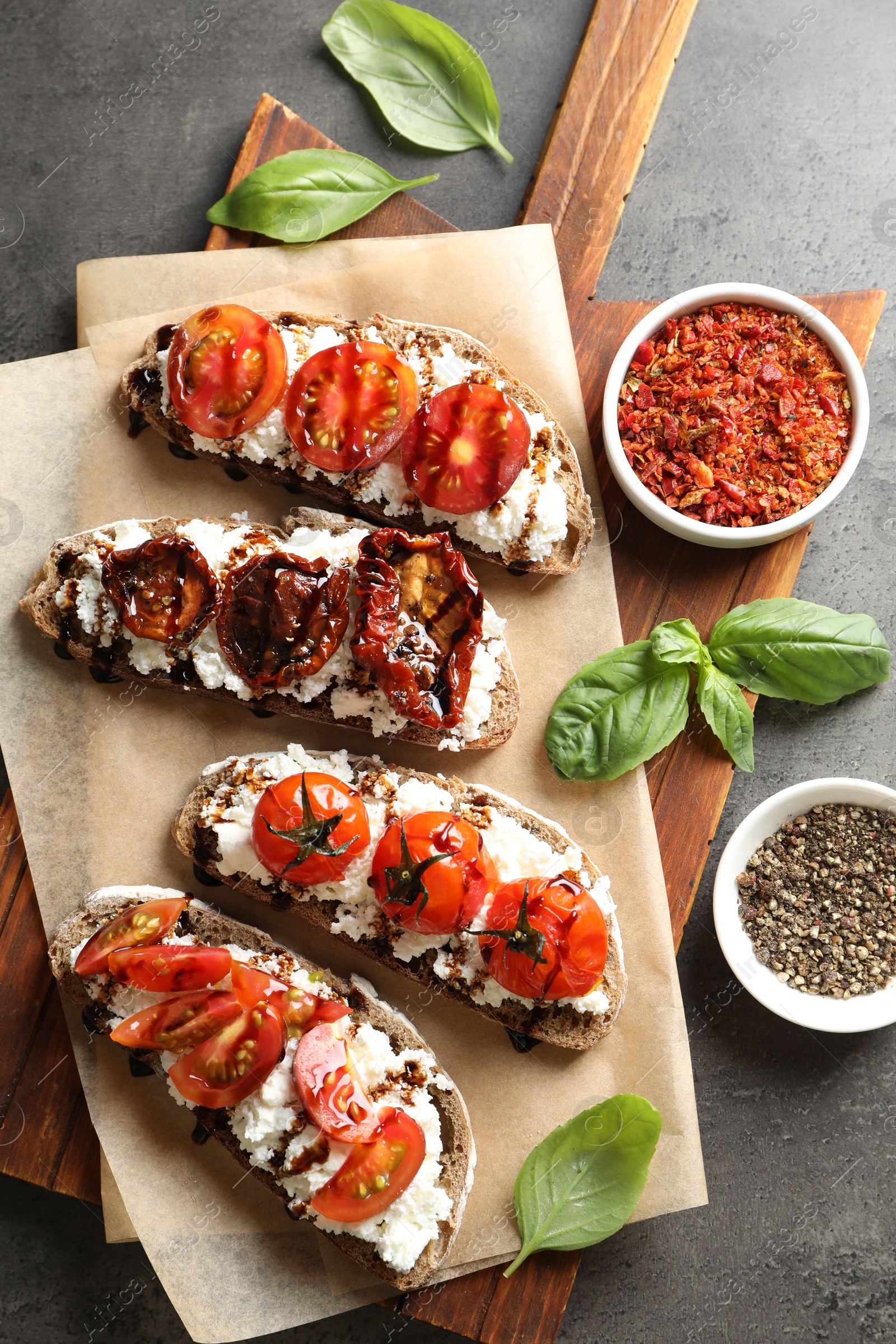 Photo of Delicious ricotta bruschettas with sun dried tomatoes, spices and basil on grey textured table, flat lay