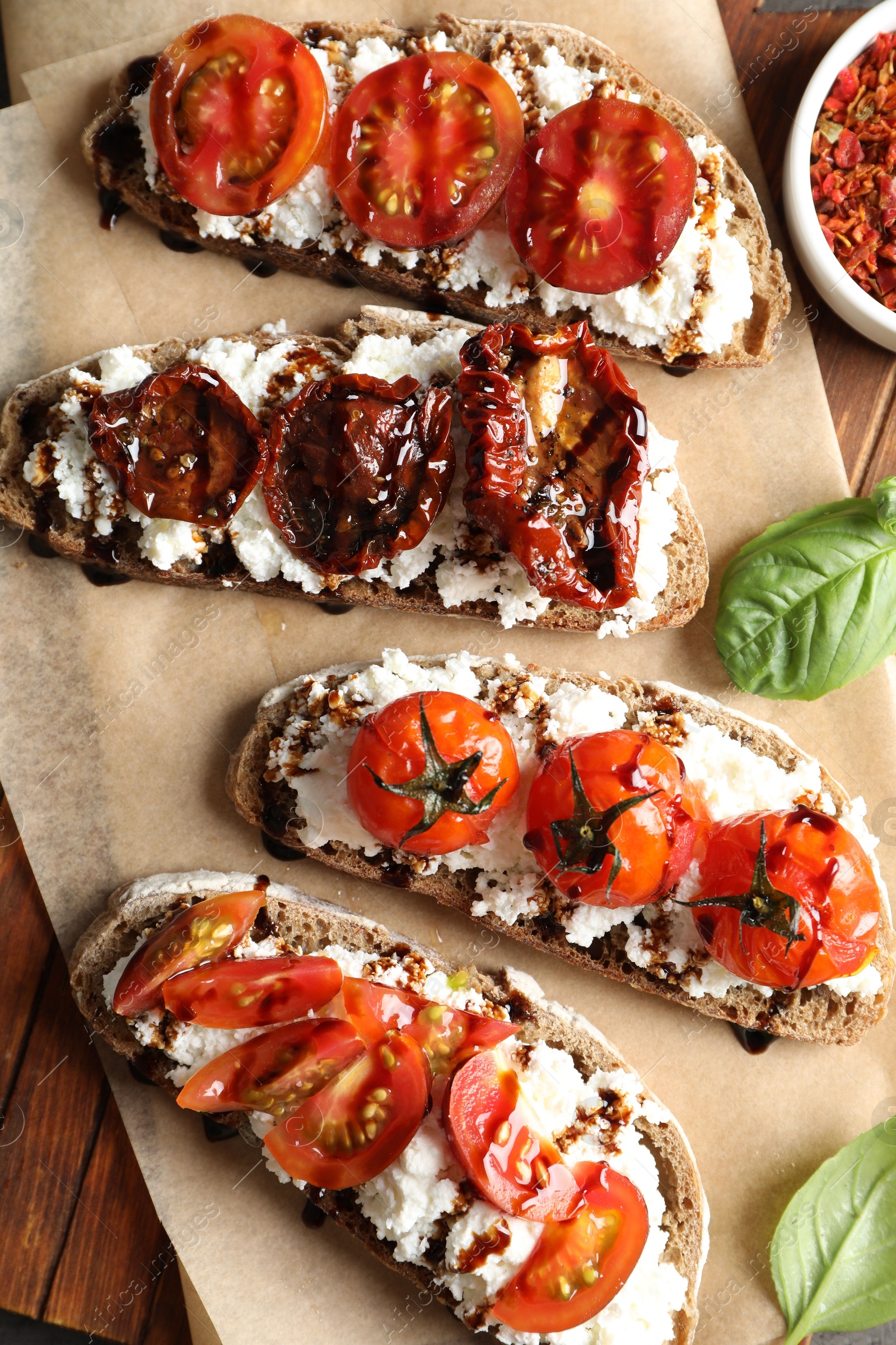 Photo of Delicious ricotta bruschettas with sun dried tomatoes, and basil on wooden table, flat lay