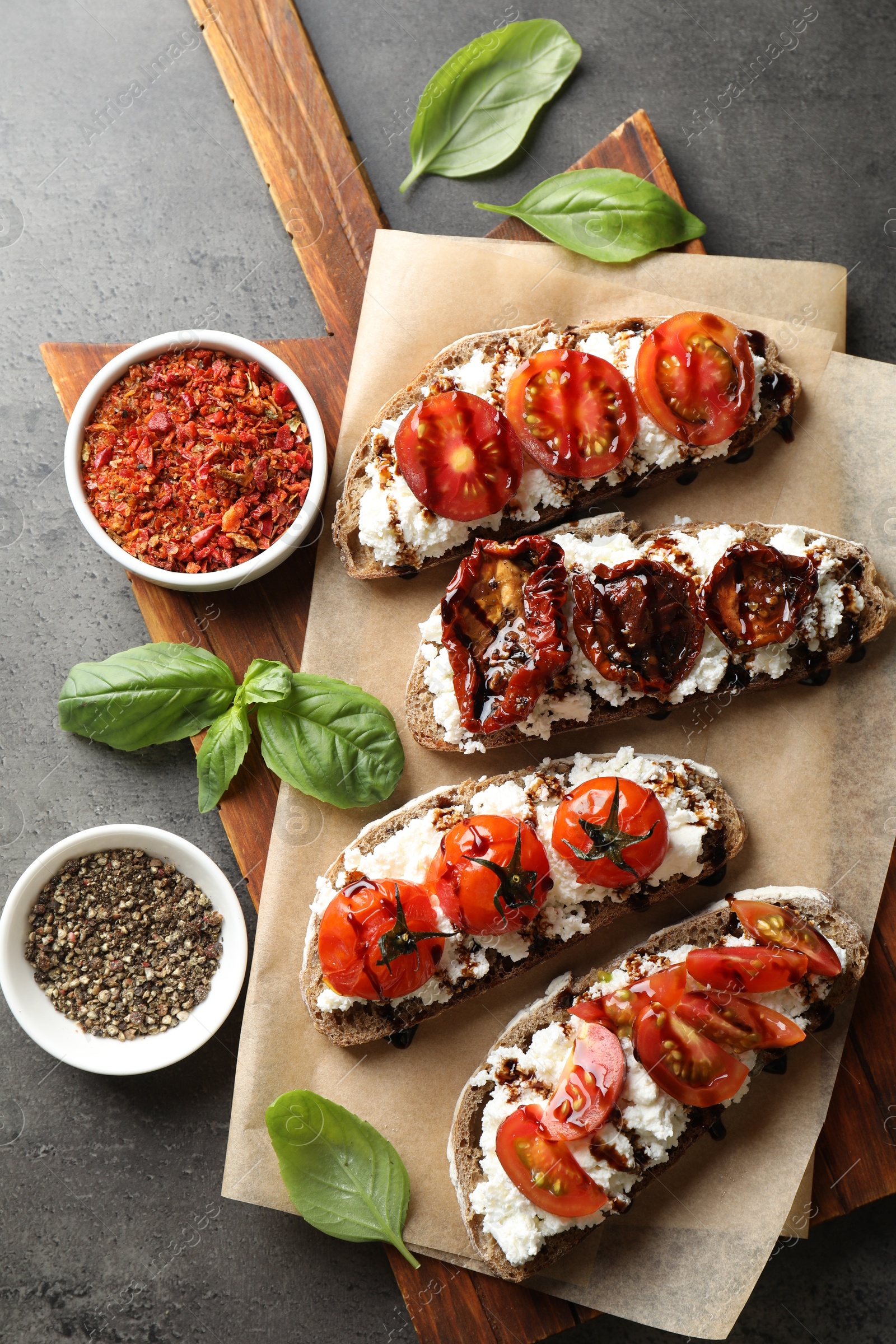 Photo of Delicious ricotta bruschettas with sun dried tomatoes, spices and basil on grey textured table, flat lay