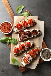 Delicious ricotta bruschettas with sun dried tomatoes, spices and basil on grey textured table, flat lay