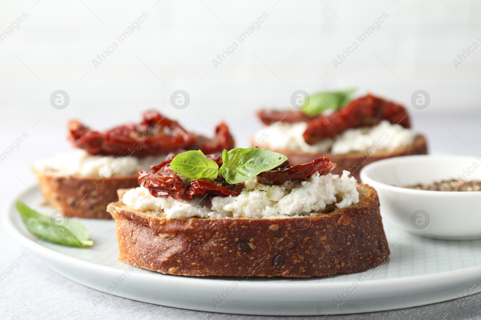 Photo of Delicious ricotta bruschettas with sun dried tomatoes and basil on light table, closeup