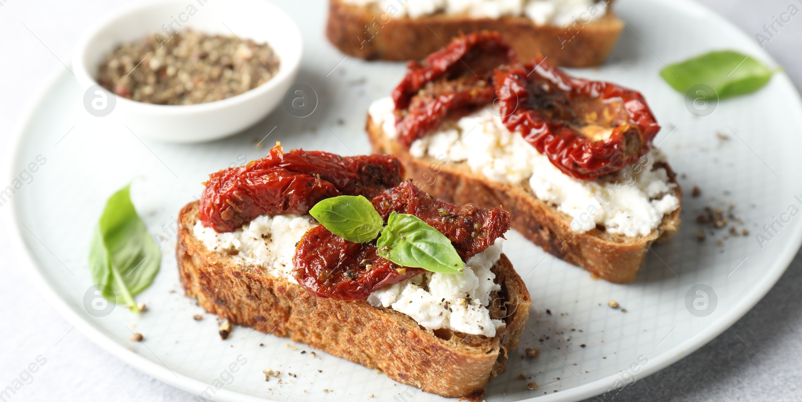 Photo of Delicious ricotta bruschettas with sun dried tomatoes, basil and milled pepper on light table, closeup