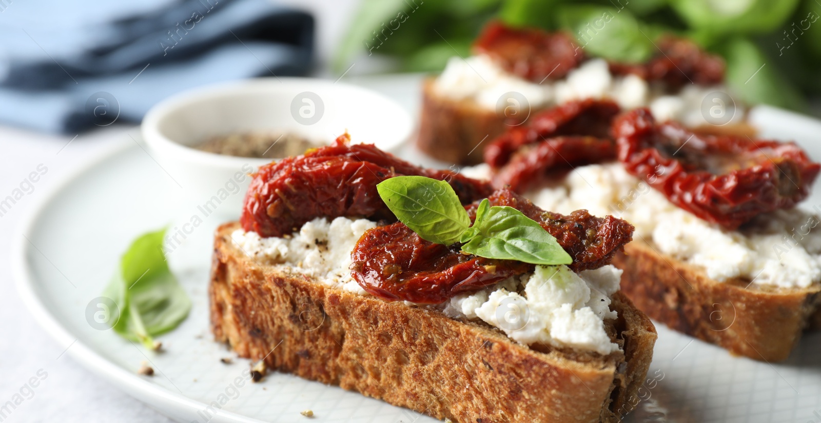 Photo of Delicious ricotta bruschettas with sun dried tomatoes, basil and milled pepper on light table, closeup