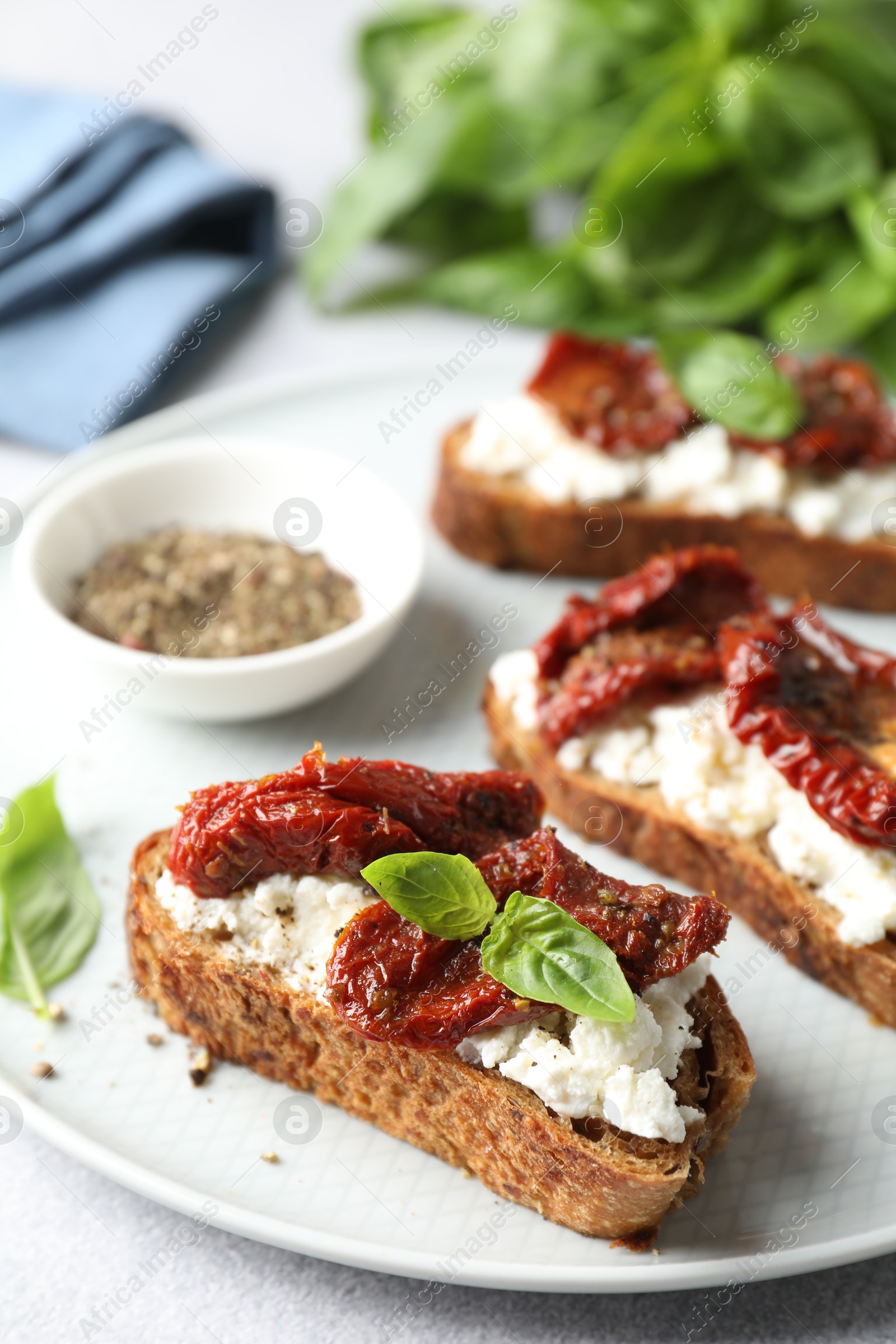 Photo of Delicious ricotta bruschettas with sun dried tomatoes, basil and milled pepper on light table, closeup