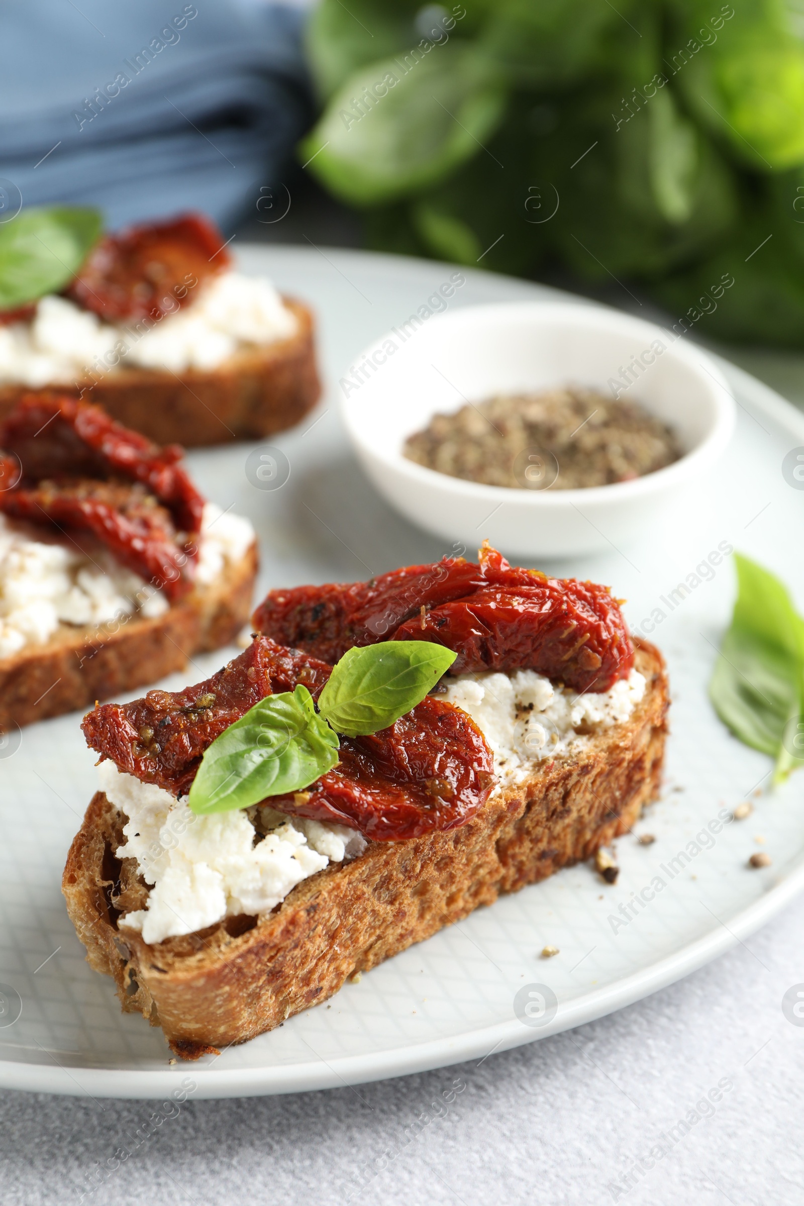 Photo of Delicious ricotta bruschettas with sun dried tomatoes, basil and milled pepper on light table, closeup