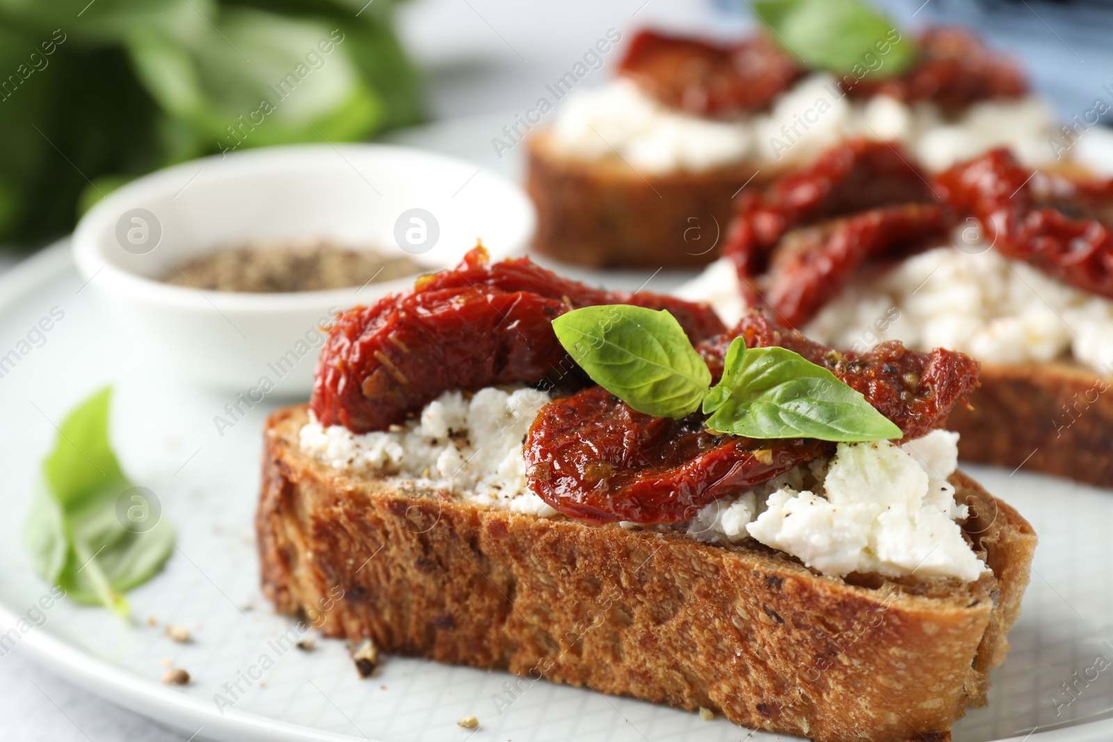 Photo of Delicious ricotta bruschetta with sun dried tomatoes, basil and milled pepper on light table, closeup