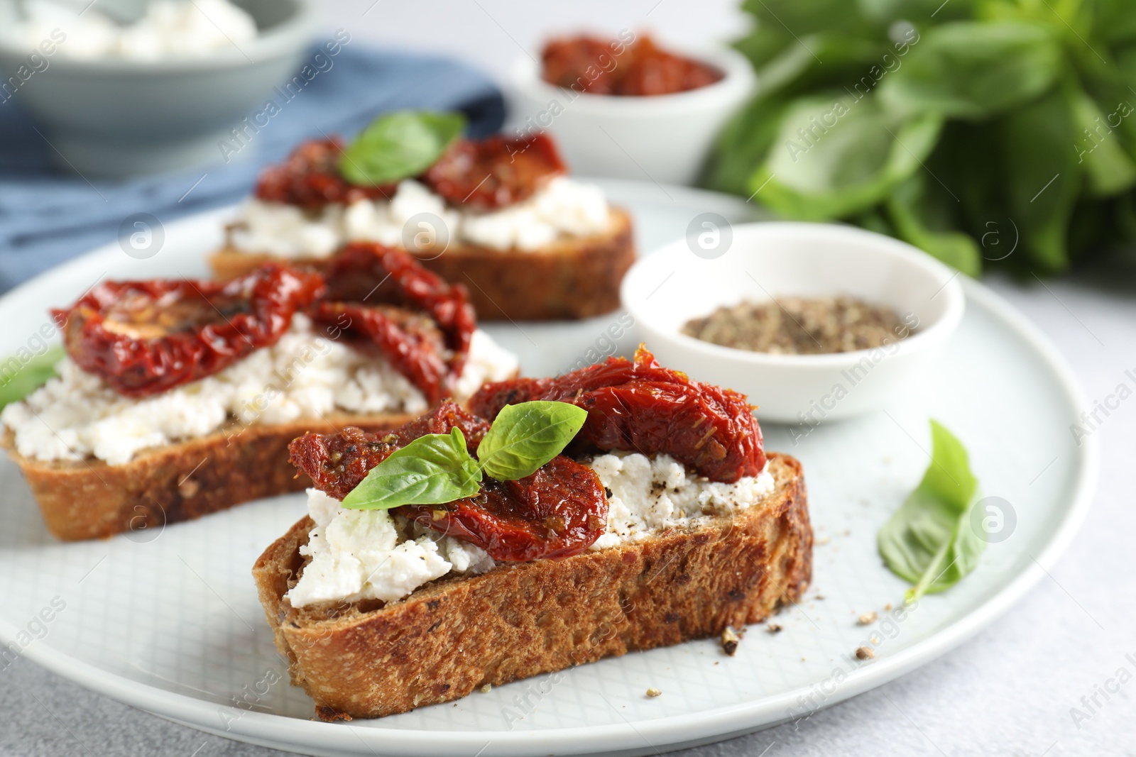 Photo of Delicious ricotta bruschettas with sun dried tomatoes, basil and milled pepper on light table, closeup