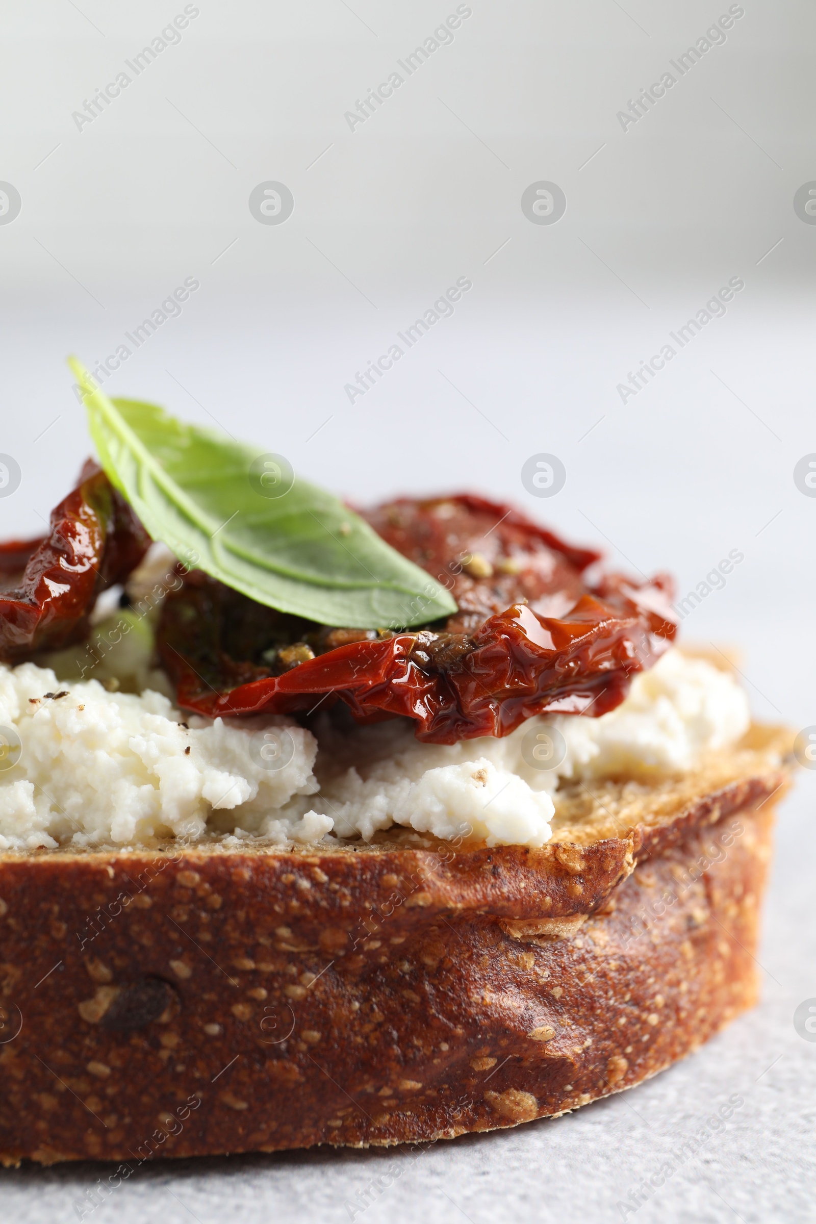 Photo of Delicious ricotta bruschetta with sun dried tomatoes and basil on light table, closeup