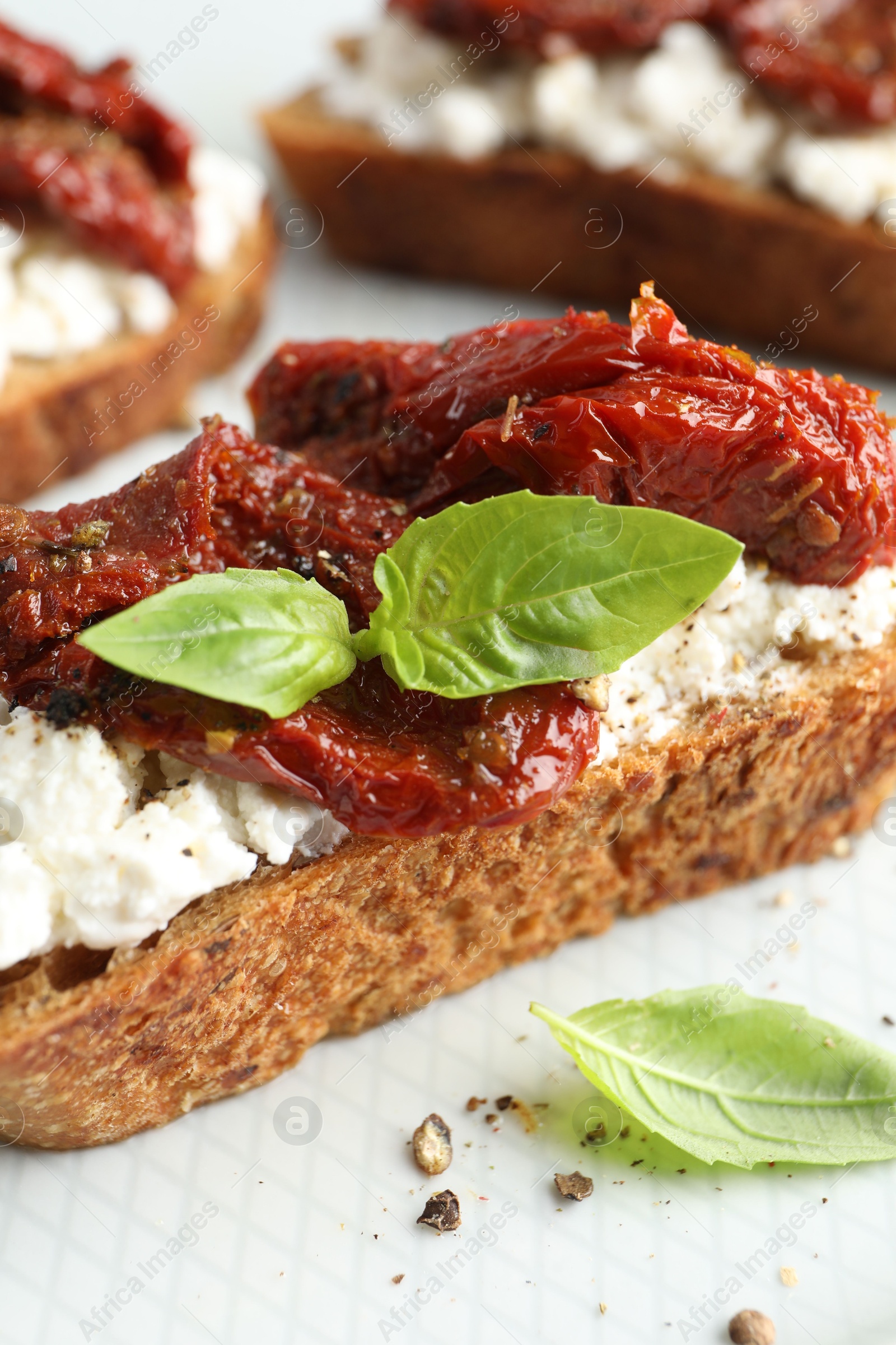 Photo of Delicious ricotta bruschetta with sun dried tomatoes and basil on plate, closeup