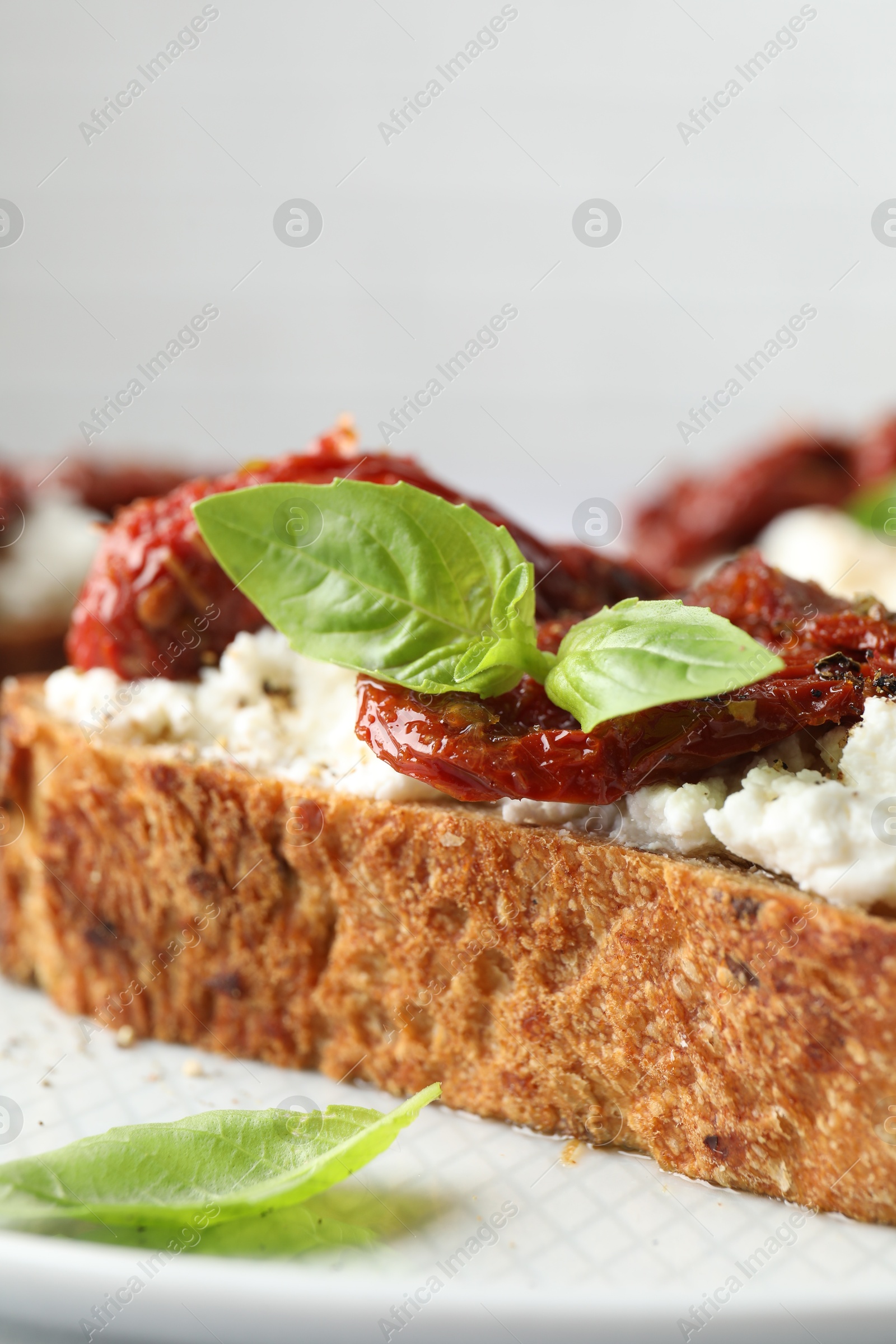 Photo of Delicious ricotta bruschetta with sun dried tomatoes and basil on plate, closeup