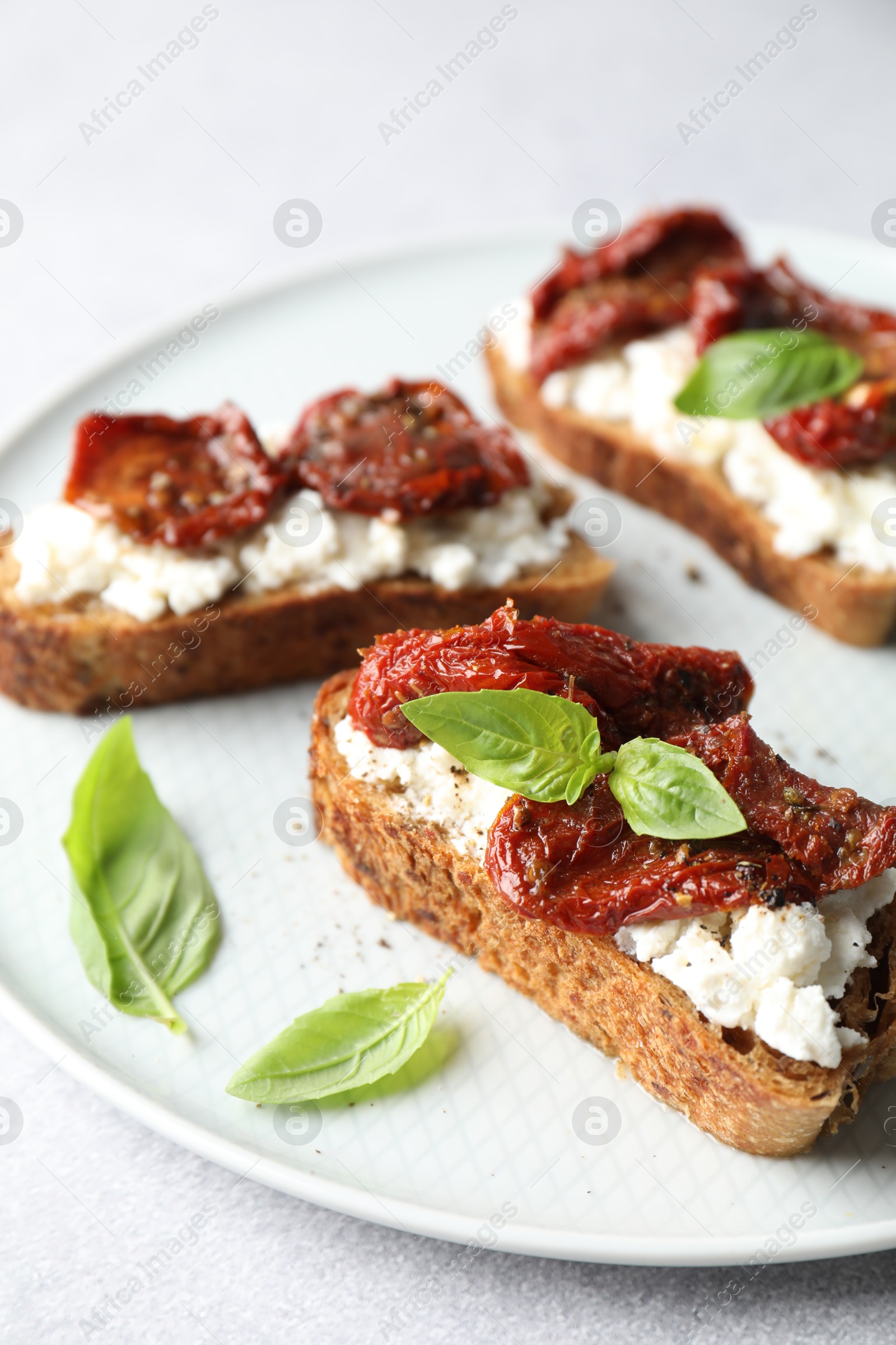 Photo of Delicious ricotta bruschettas with sun dried tomatoes and basil on light table, closeup