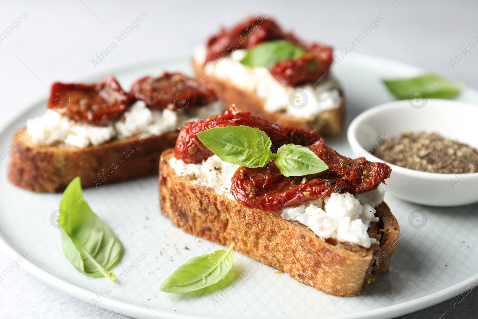 Photo of Delicious ricotta bruschettas with sun dried tomatoes, basil and milled pepper on light table, closeup