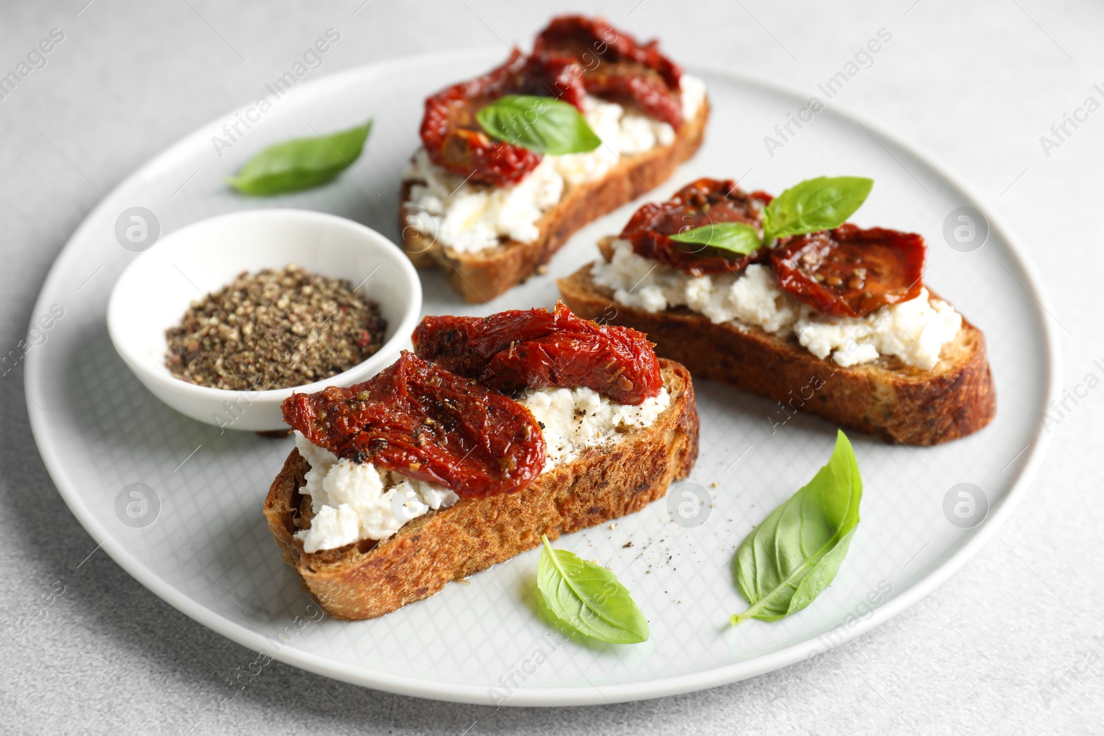 Photo of Delicious ricotta bruschettas with sun dried tomatoes, basil and milled pepper on light table, closeup