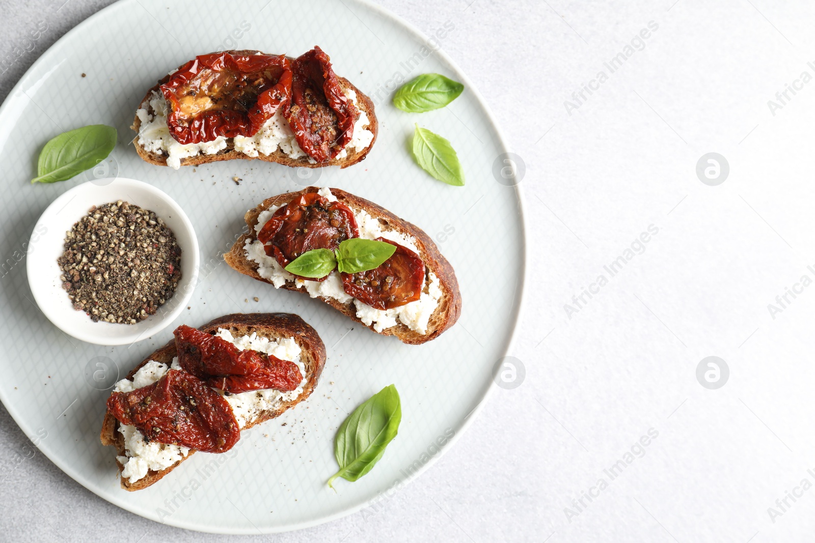 Photo of Delicious ricotta bruschettas with sun dried tomatoes, basil and milled pepper on light table, top view. Space for text