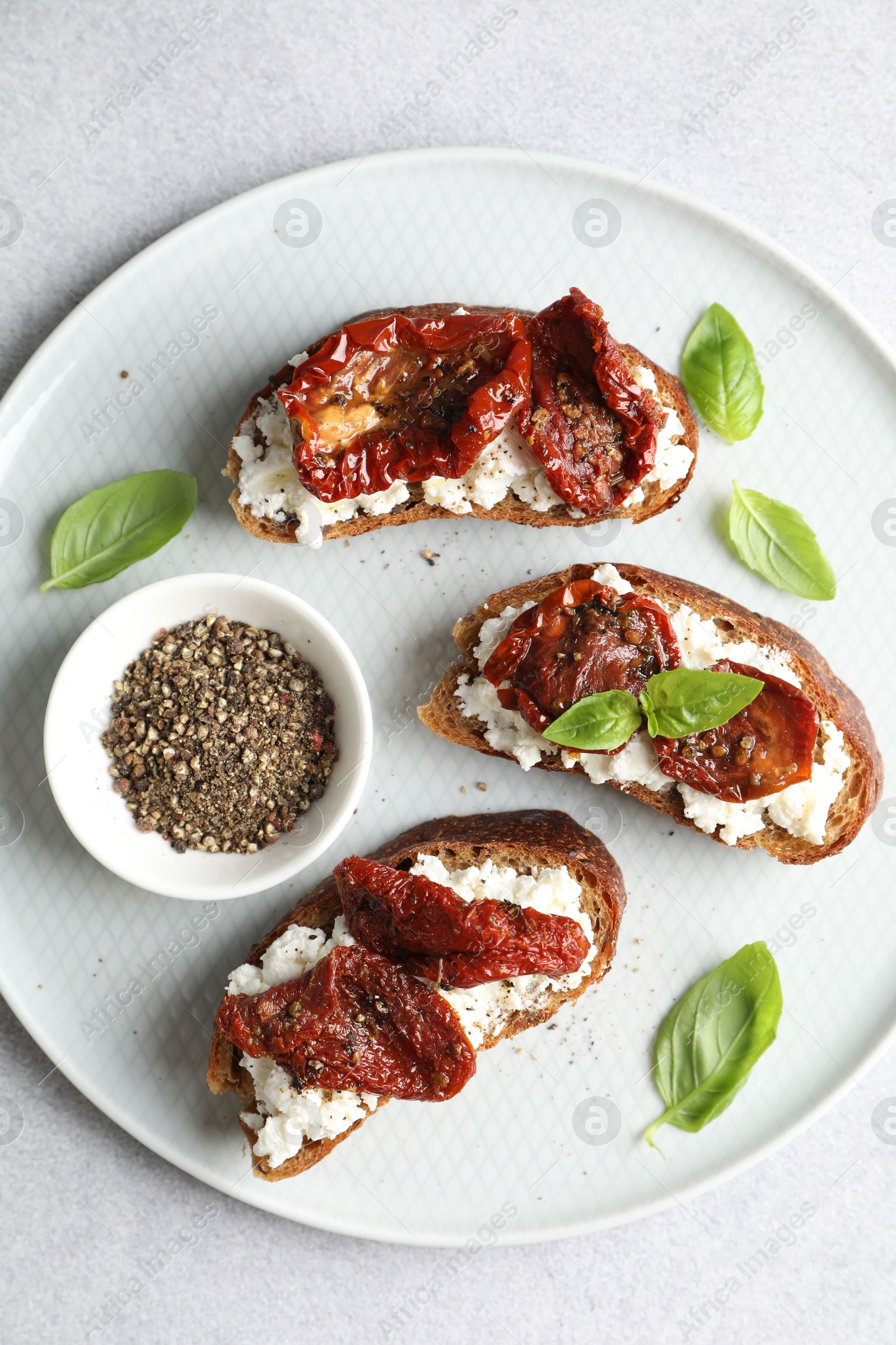 Photo of Delicious ricotta bruschettas with sun dried tomatoes, basil and milled pepper on light table, top view