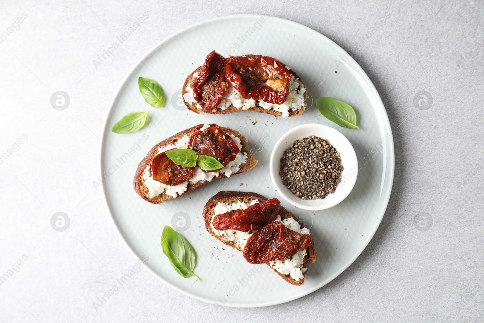 Photo of Delicious ricotta bruschettas with sun dried tomatoes, basil and milled pepper on light table, top view