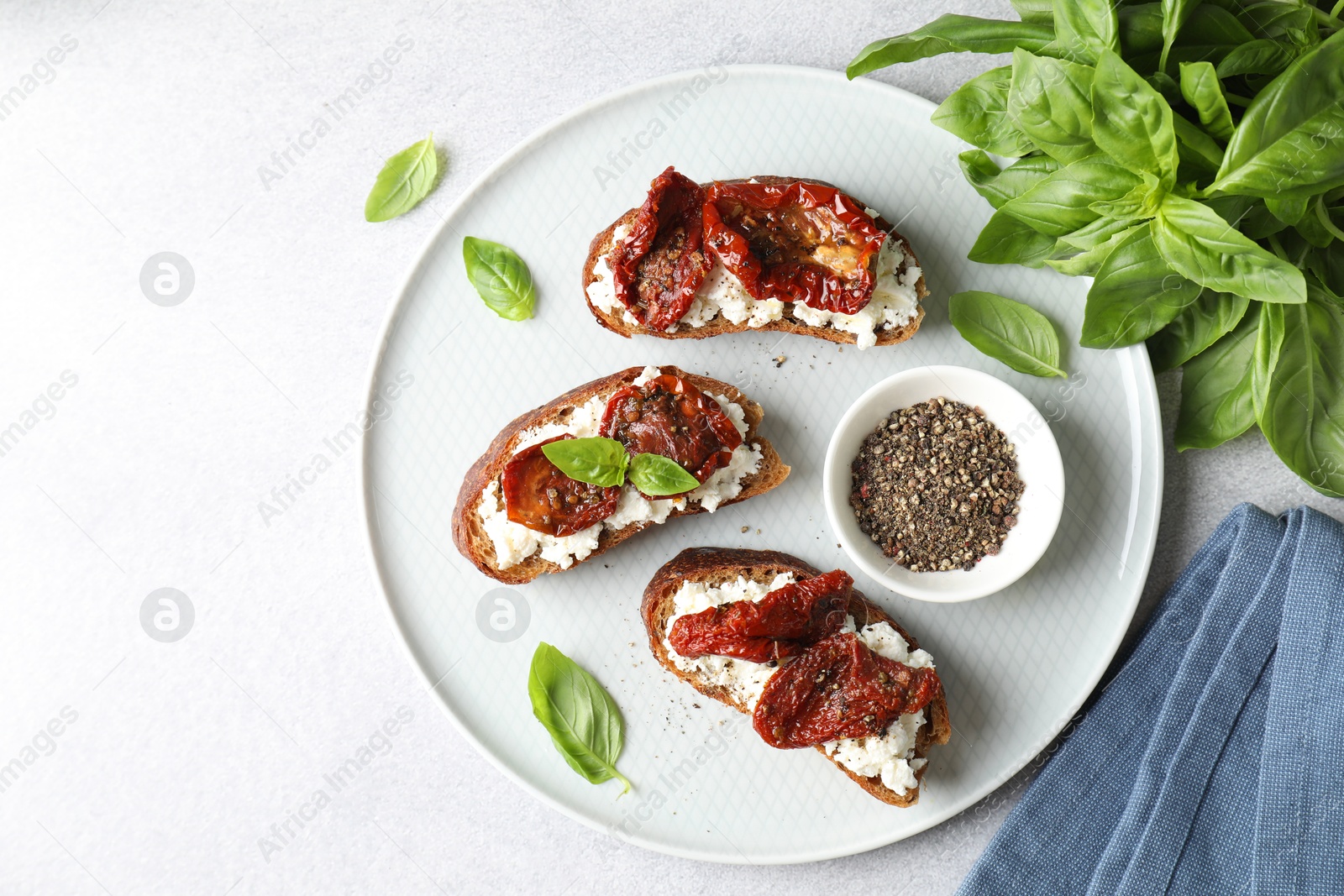 Photo of Delicious ricotta bruschettas with sun dried tomatoes, basil and milled pepper on light table, flat lay. Space for text