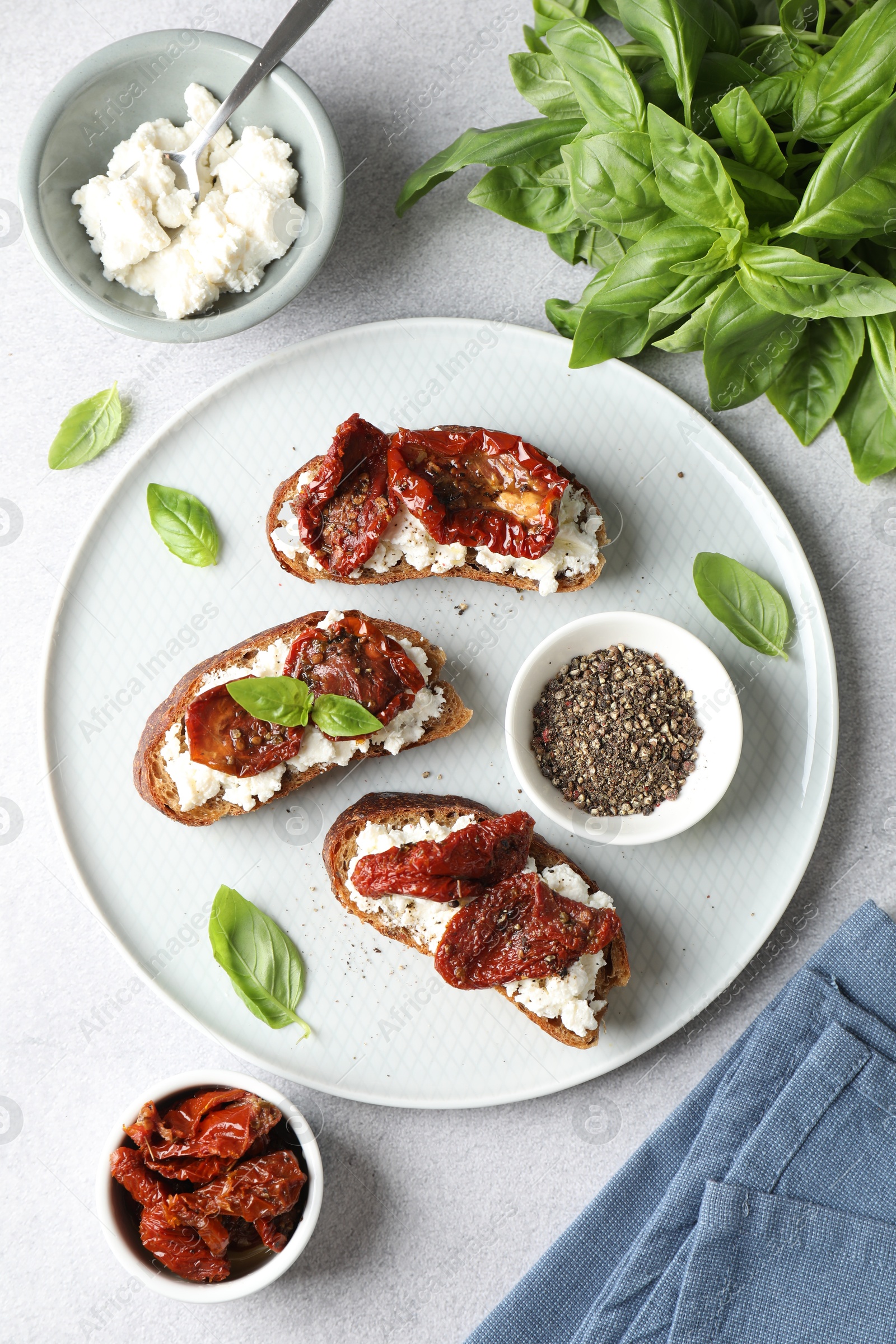 Photo of Delicious ricotta bruschettas with sun dried tomatoes, basil and milled pepper on light table, flat lay