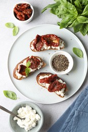 Photo of Delicious ricotta bruschettas with sun dried tomatoes, basil and milled pepper on light table, flat lay