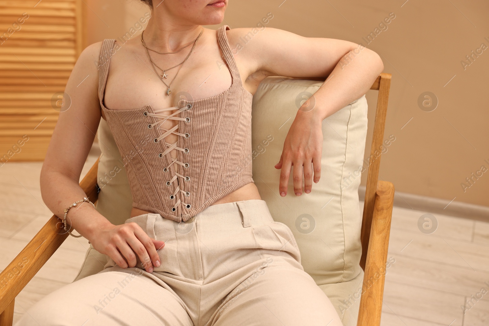 Photo of Woman in stylish corset on armchair indoors, closeup