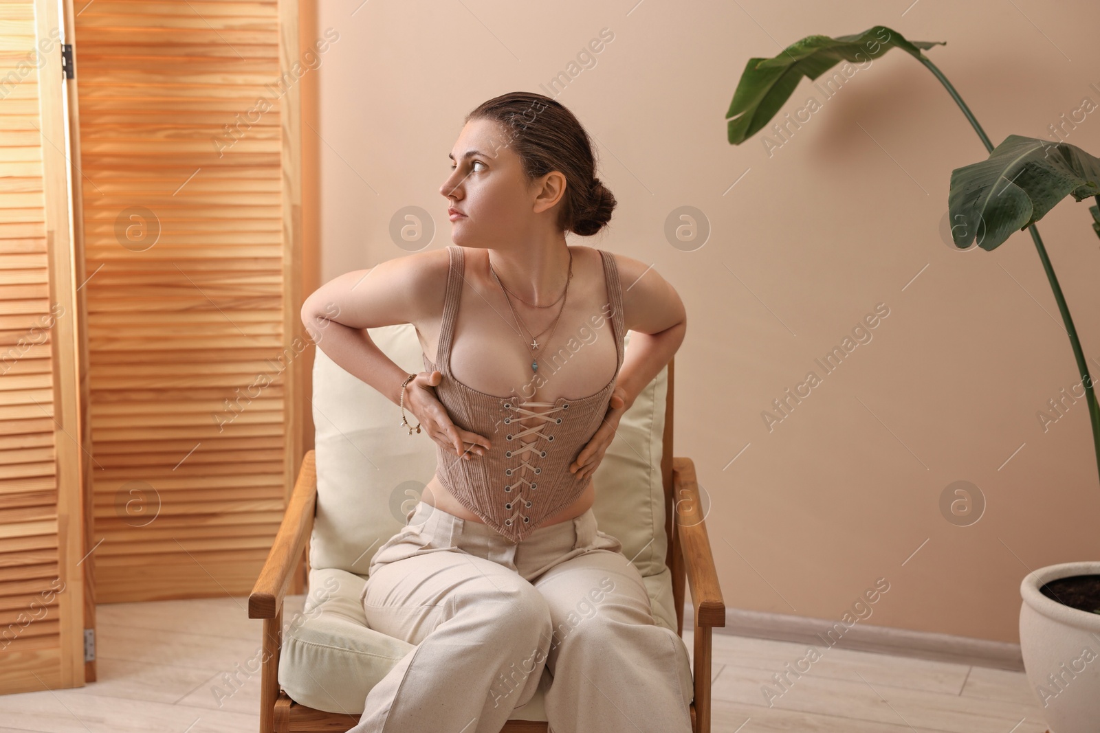 Photo of Beautiful woman in stylish corset on armchair indoors