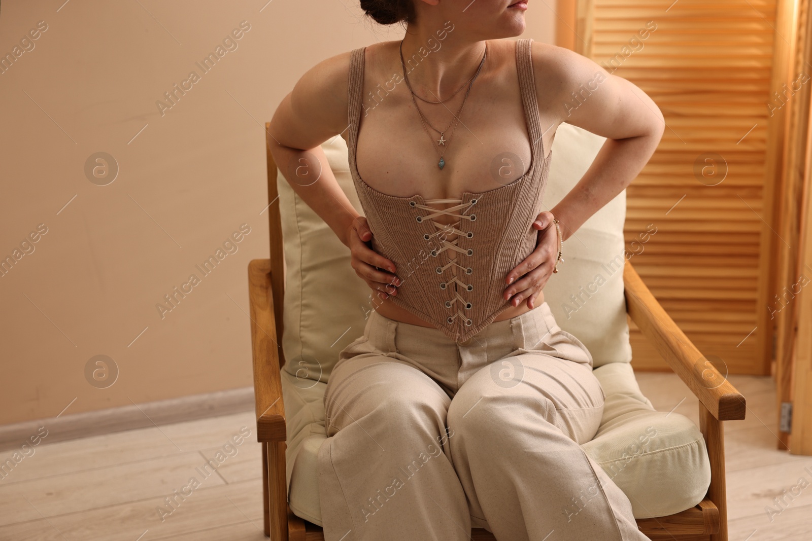 Photo of Woman in stylish corset on armchair indoors, closeup