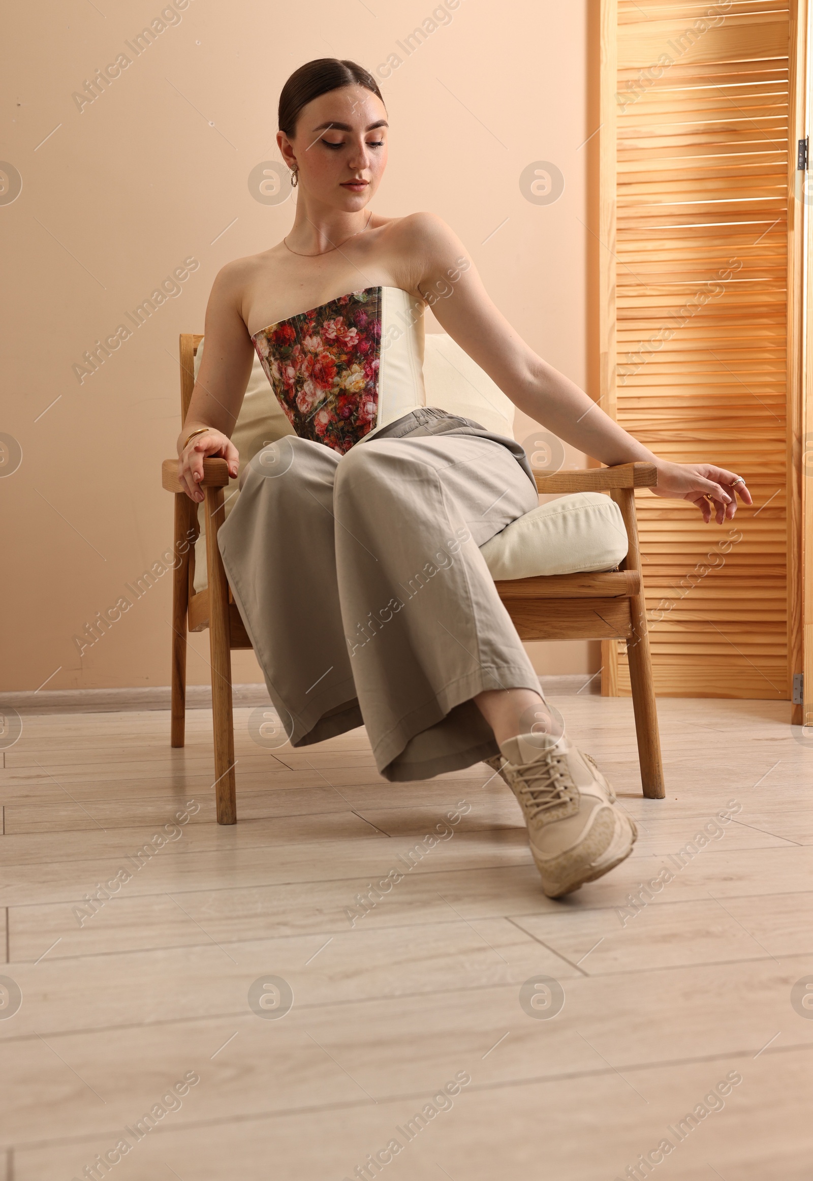 Photo of Beautiful young woman in stylish corset on armchair indoors