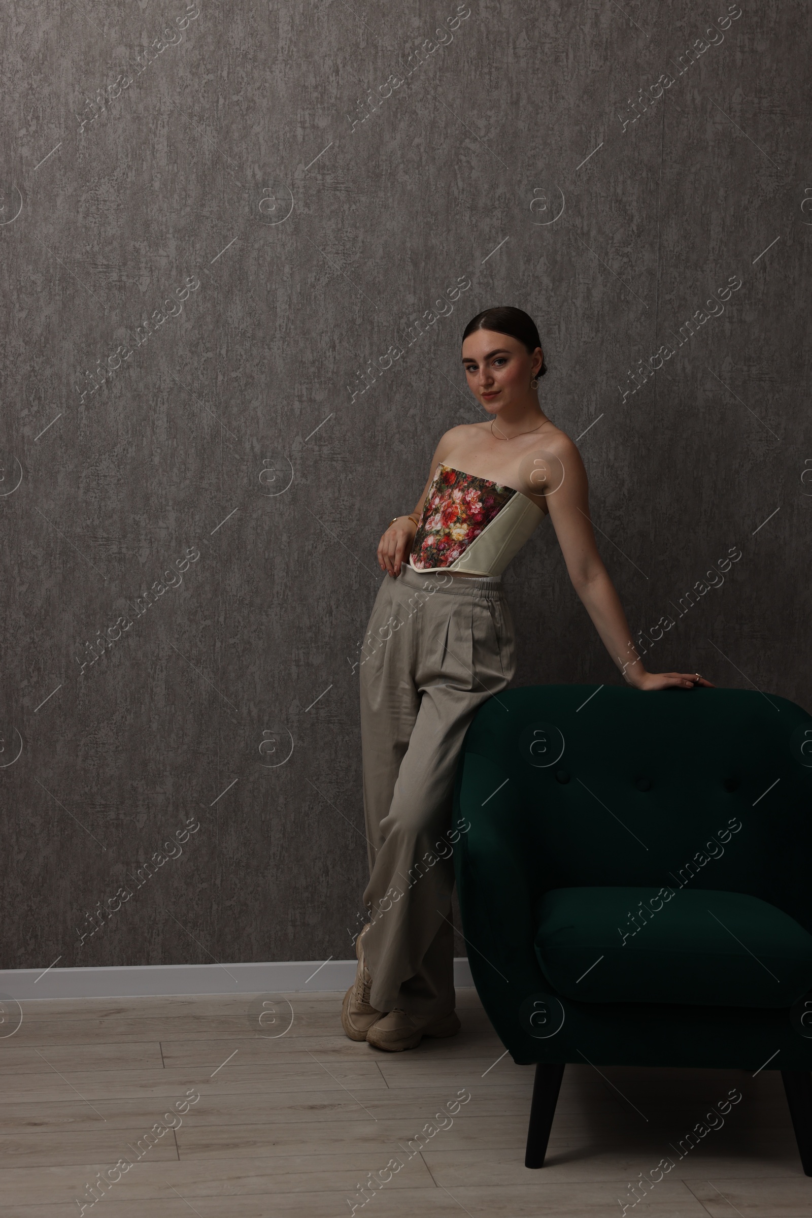 Photo of Beautiful young woman in stylish corset near armchair indoors