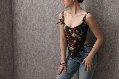 Photo of Woman in stylish corset near grey wall, closeup. Space for text