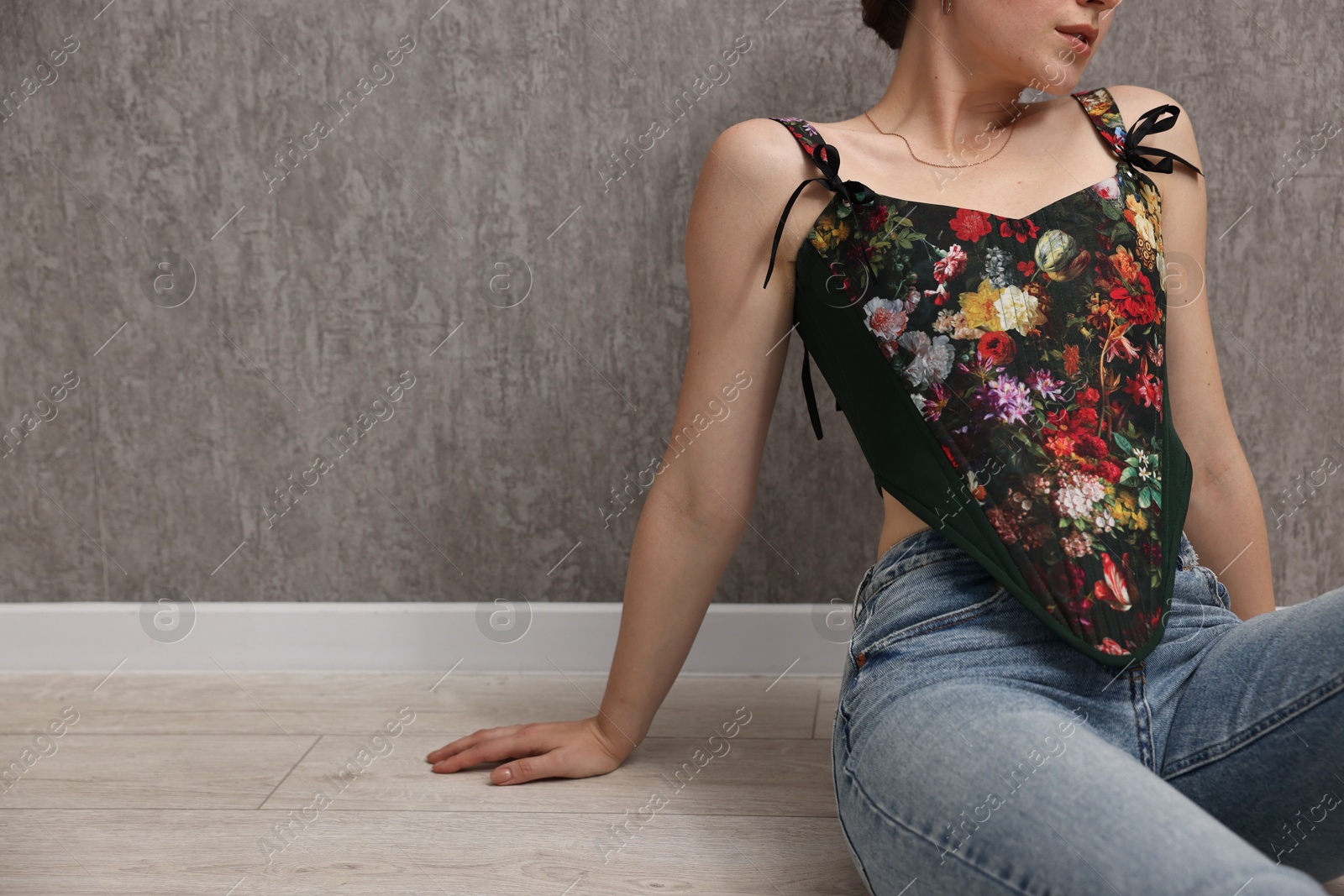 Photo of Woman in stylish corset on floor near grey wall, closeup