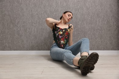 Photo of Beautiful young woman in stylish corset on floor near grey wall