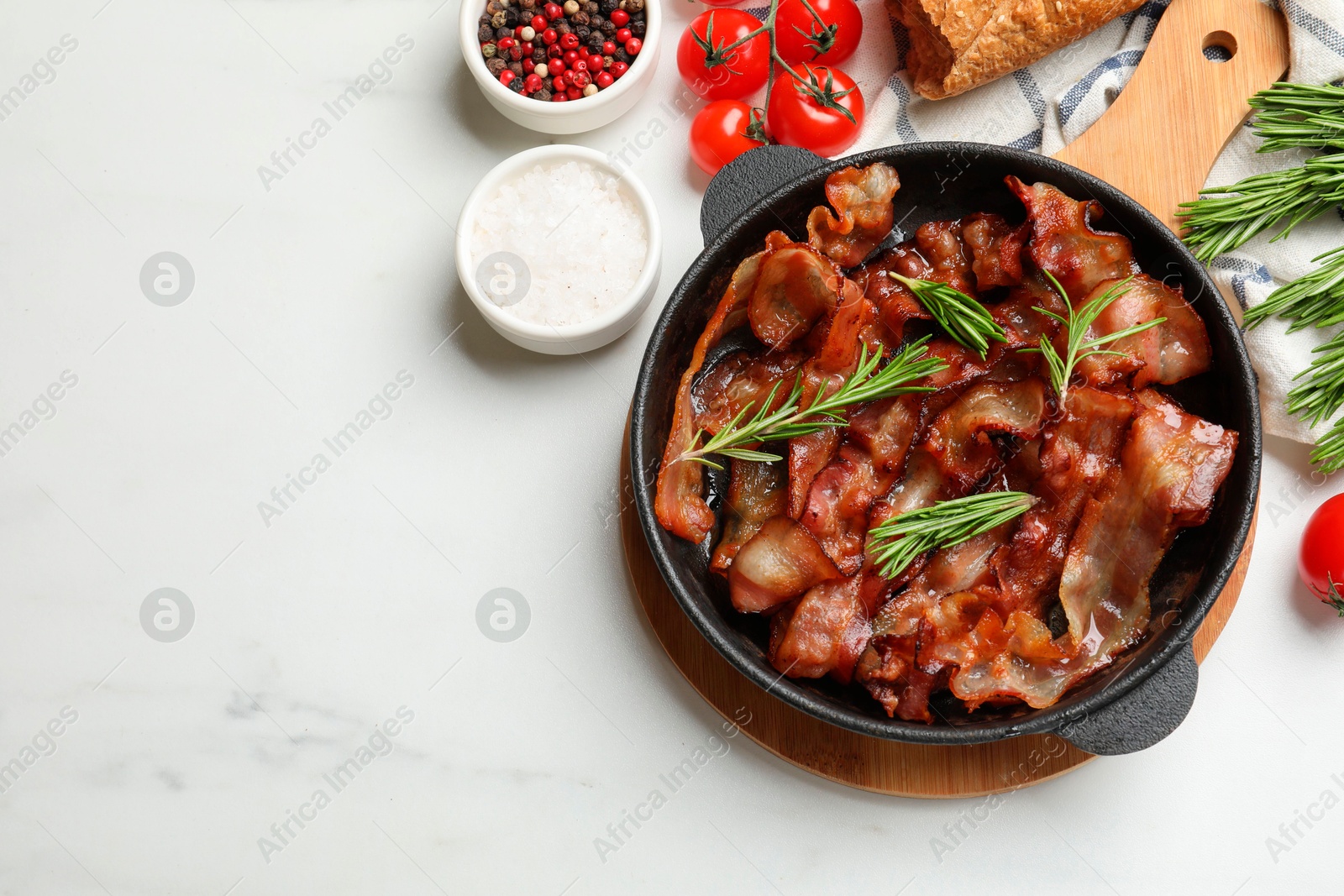 Photo of Delicious bacon slices in frying pan, spices and tomatoes on white table, flat lay. Space for text