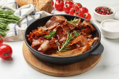 Photo of Delicious bacon slices in frying pan, spices and tomatoes on white table