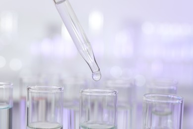 Photo of Dripping liquid from pipette into test tube on light background, closeup