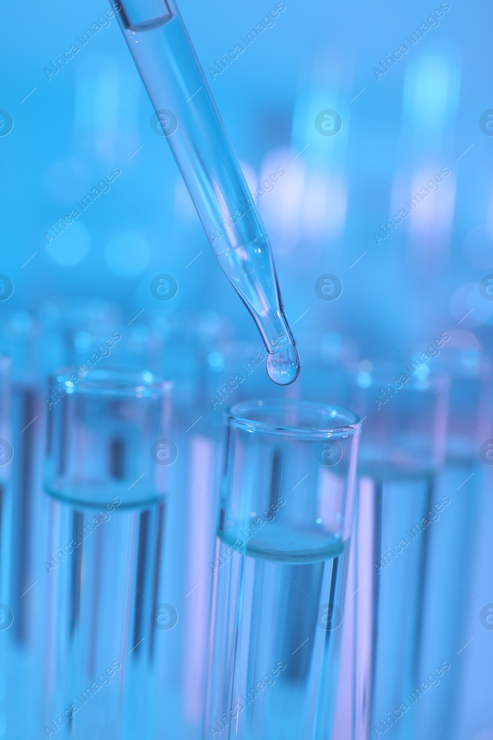 Photo of Dripping liquid from pipette into test tube on light blue background, closeup