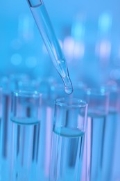 Photo of Dripping liquid from pipette into test tube on light blue background, closeup