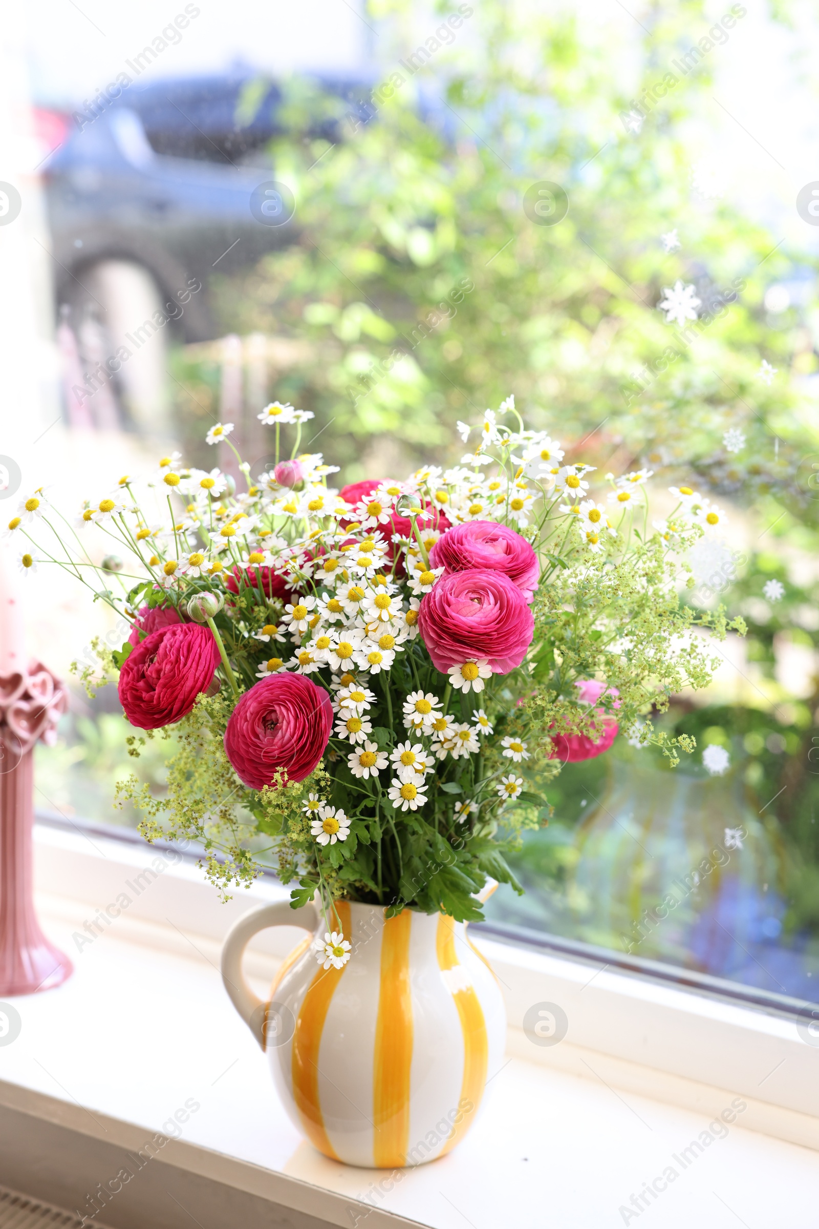 Photo of Beautiful ranunculus flowers and chamomiles in vase on windowsill indoors