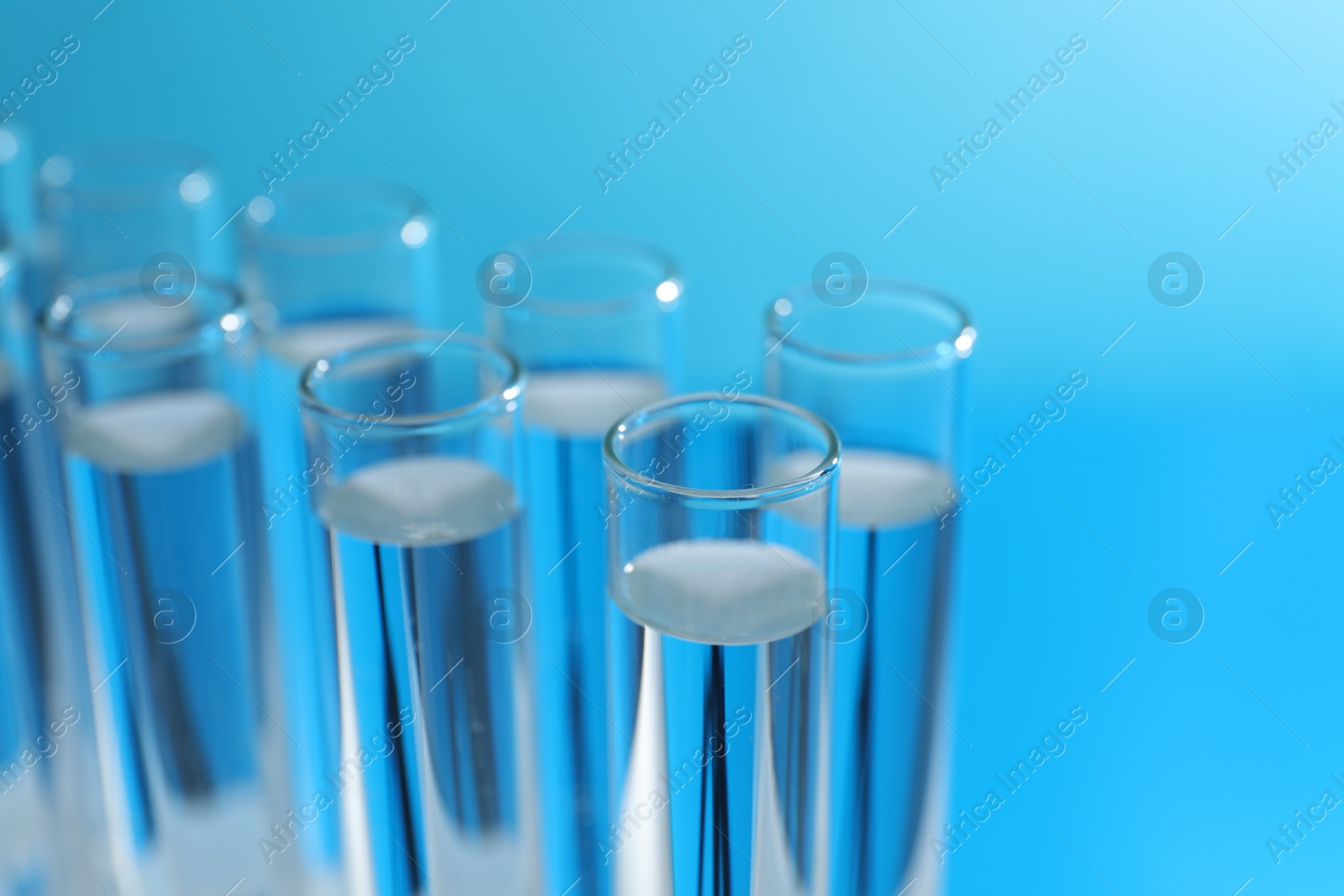 Photo of Many glass test tubes on light blue background, closeup