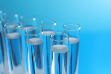 Photo of Many glass test tubes on light blue background, closeup