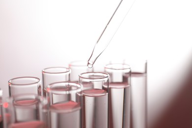 Dripping liquid from pipette into test tube on light background, closeup