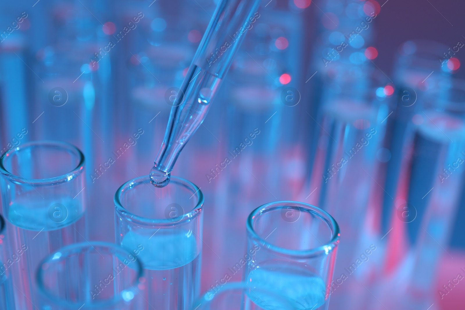 Photo of Dripping liquid from pipette into test tube on color background, closeup