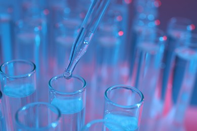 Dripping liquid from pipette into test tube on color background, closeup