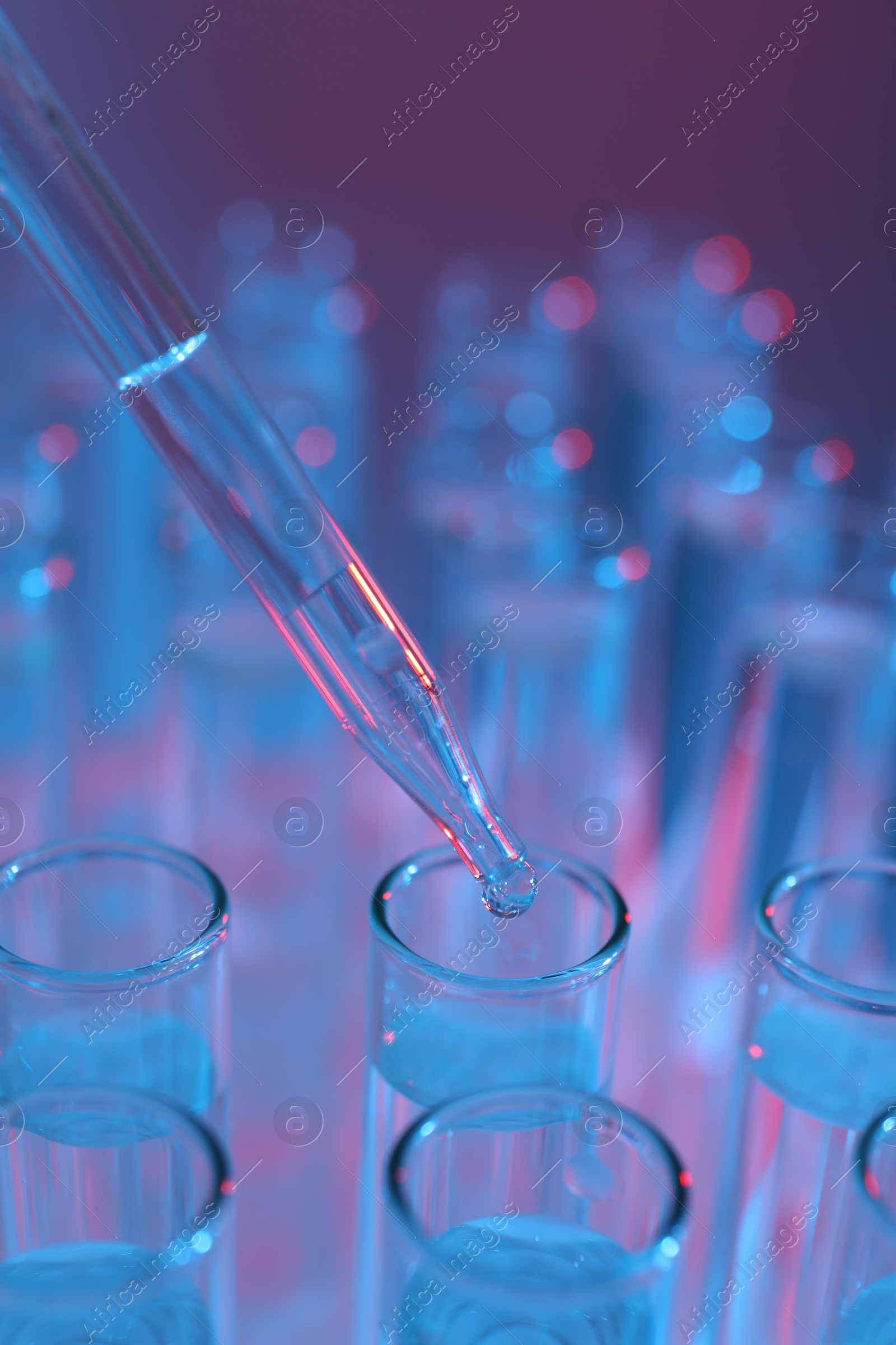 Photo of Dripping liquid from pipette into test tube on color background, closeup