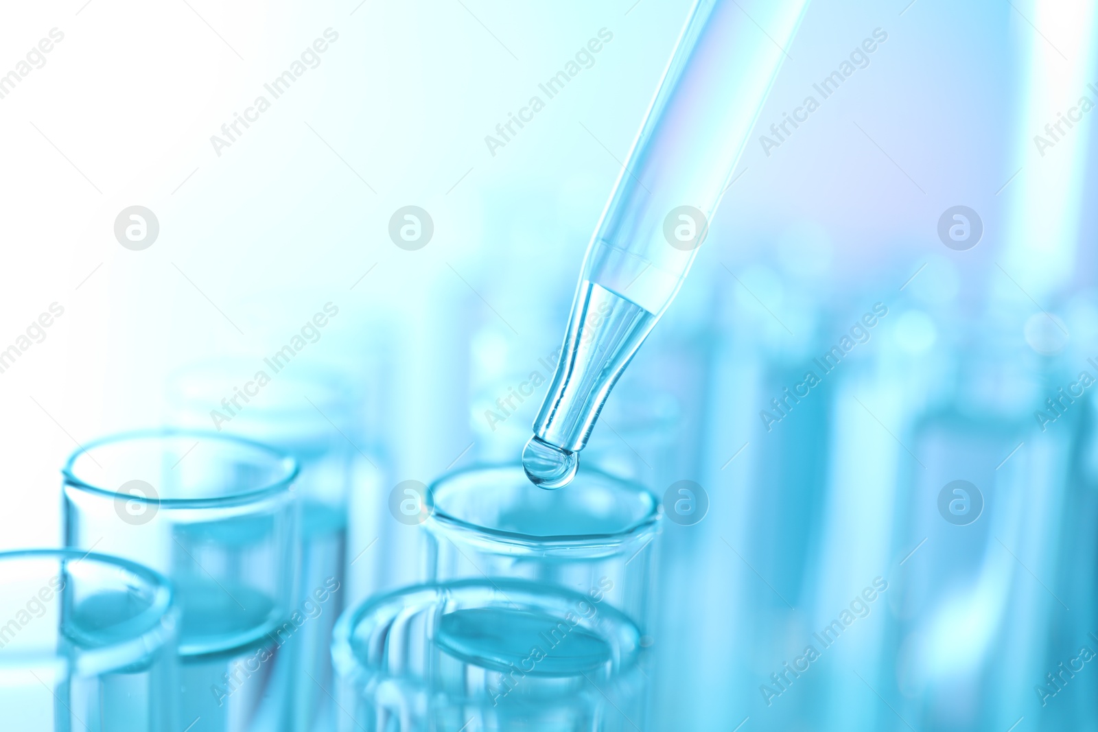 Photo of Dripping liquid from pipette into test tube on light blue background, closeup