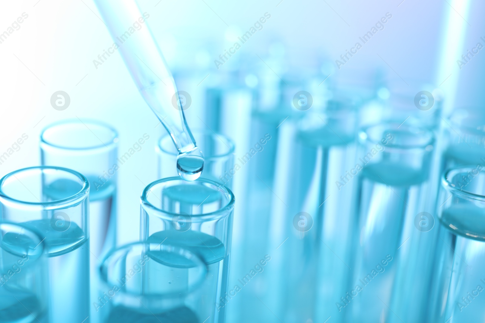 Photo of Dripping liquid from pipette into test tube on light blue background, closeup