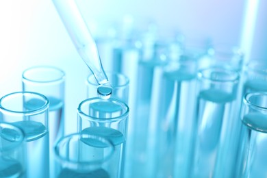 Dripping liquid from pipette into test tube on light blue background, closeup