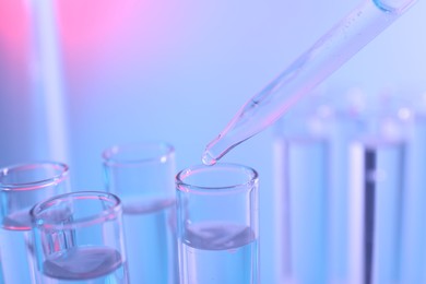 Photo of Dripping liquid from pipette into test tube on color background, closeup