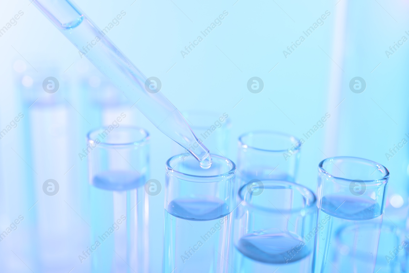 Photo of Dripping liquid from pipette into test tube on light blue background, closeup