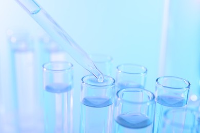 Dripping liquid from pipette into test tube on light blue background, closeup