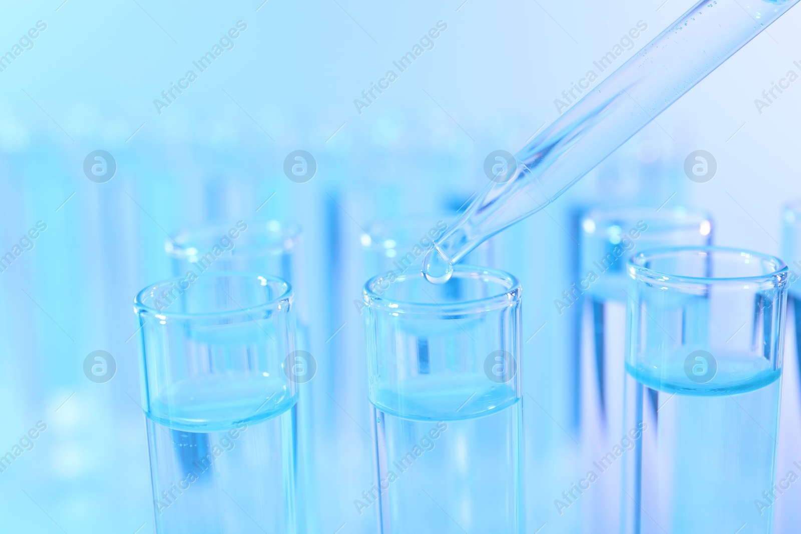 Photo of Dripping liquid from pipette into test tube on light blue background, closeup